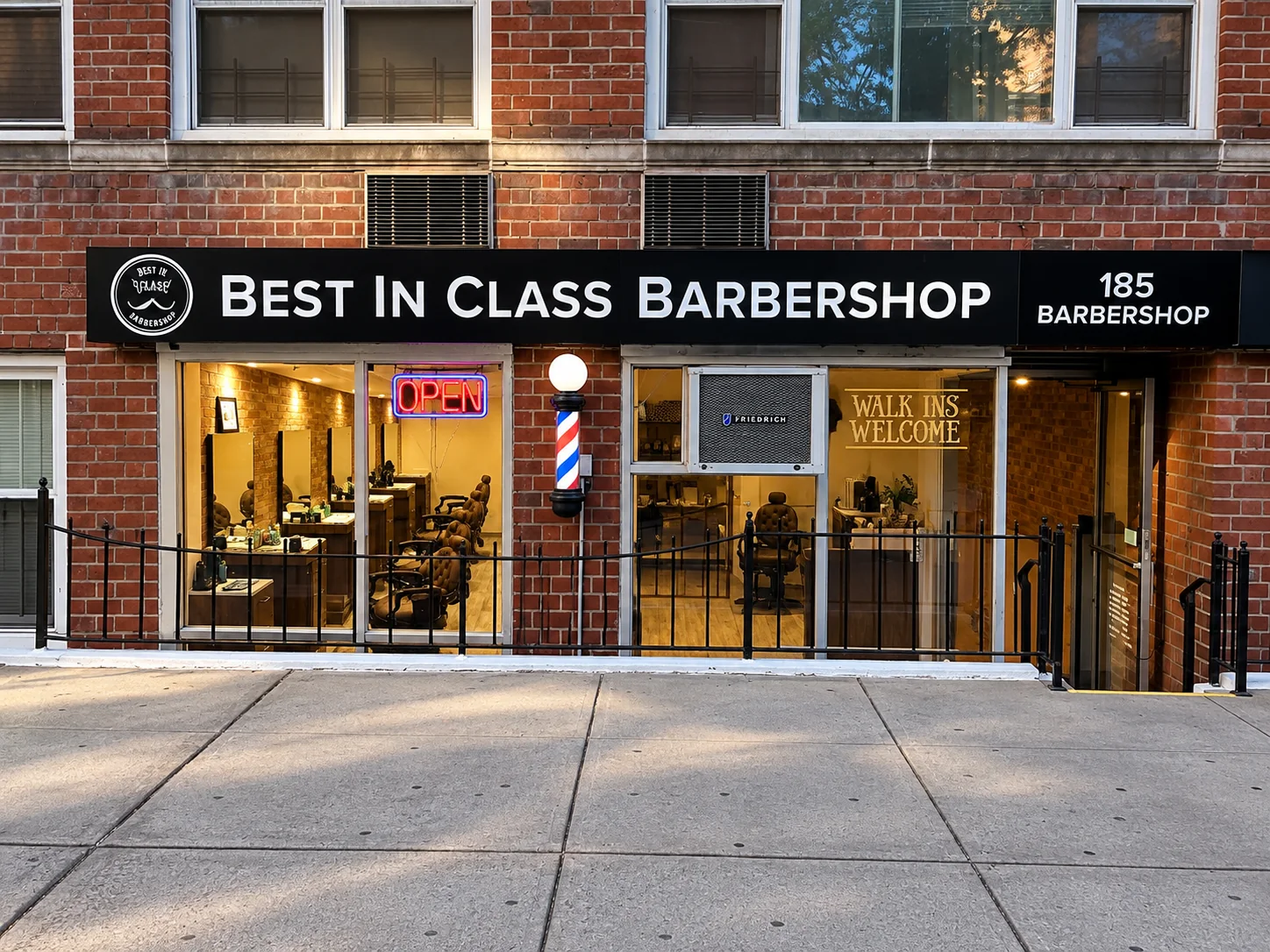 The Best In Class Barbershop storefront at 185 6th Avenue: black sign with the shop logo, red brick, a barber pole, a neon Open sign and a Walk Ins Welcome window.